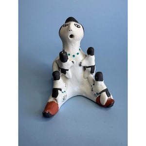 Puede incluir: Figurita de cerámica pintada a mano de una mujer con tres niños, todos con cabello y ojos negros, y cuerpos blancos con detalles negros y turquesa.