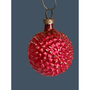 May include: A vintage red Christmas ornament with a textured, bumpy surface and a metallic gold cap. The ornament is suspended by a silver wire loop, perfect for holiday decorating. The red color is vibrant and eye-catching.