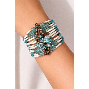 May include: A multi-strand bracelet featuring white, turquoise, and clear beads. The bracelet has a central cluster of decorative stones in shades of blue, green, and brown. The bracelet is worn on a wrist.