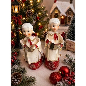May include: Two vintage Christmas choir boy figurines. The figurines wear white robes with red accents and hold songbooks. The scene includes a miniature snow-covered house, a lamppost, and red ornaments. A sign reads "Merry Christmas."