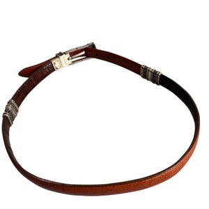 Peut inclure: Une ceinture en cuir marron &agrave; la surface textur&eacute;e, dot&eacute;e d'une boucle en m&eacute;tal argent&eacute; et de deux ornements d&eacute;coratifs en m&eacute;tal argent&eacute; plac&eacute;s le long de la sangle. La ceinture pr&eacute;sente une fermeture &agrave; ardillon classique et une doublure int&eacute;rieure lisse.
