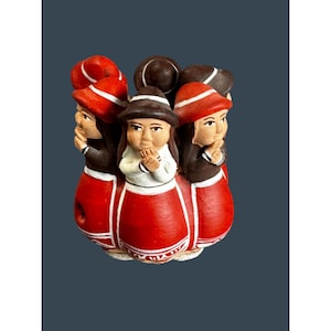 Puede incluir: Una figura de cerámica con múltiples figuras vestidas con trajes tradicionales. Las figuras visten faldas rojas, chaquetas negras y sombreros rojos y marrones. Los rostros son detallados y el diseño es colorido y decorativo.