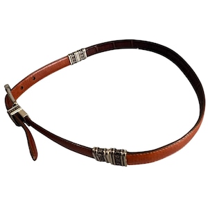 Peut inclure: Une ceinture en cuir marron dot&eacute;e d'une boucle en m&eacute;tal argent&eacute; et de deux ornements d&eacute;coratifs en m&eacute;tal argent&eacute; le long de la sangle. La ceinture pr&eacute;sente une finition lisse &agrave; l'ext&eacute;rieur et une doublure int&eacute;rieure marron fonc&eacute; avec des coutures.