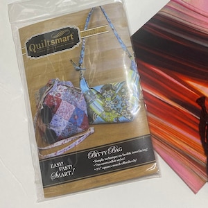 May include: Quiltsmart Bitty Bag sewing kit with fabric scraps in shades of blue, red, and pink, black cord, and instructions. Easy, Fast, Smart!