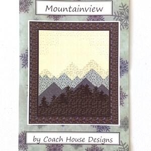 May include: A printed card featuring a mountain landscape quilt design. The quilt design has a light yellow sky, layered blue and gray mountains, and a dark brown forest. The card is titled "Mountainview" and is by "Coach House Designs". The background has a snowflake pattern.