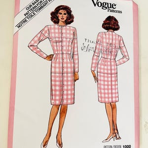 Op de afbeelding: Een Vogue Patterns naaipatroon-envelop voor een jurk met lange mouwen en een roze-wit gingham ruitpatroon. De illustratie toont voor- en achteraanzichten van de jurk, met de tekst Our Basic Pattern For Fit en patroonnummer 1000.