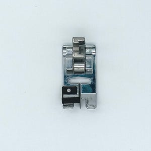 Puede incluir: Un prensatelas plateado para máquina de coser, diseñado para dobladillos. Tiene una base rectangular, una parte superior curvada y una pequeña pieza negra. Está diseñado para acoplarse a una máquina de coser.