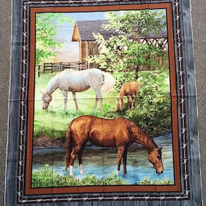 May include: Fabric panel depicting a rural scene with three horses grazing near a stream and a barn. The artwork is framed by a brown border and a faux wood and barbed wire design.