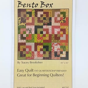 Op de afbeelding: Een gedrukt patroon voor een "Bento Box" quilt, met een patchwork ontwerp in tinten rood, groen en bruin. De quilt meet 114 cm x 114 cm en wordt beschreven als gemakkelijk en geschikt voor restjes, ideaal voor beginners.