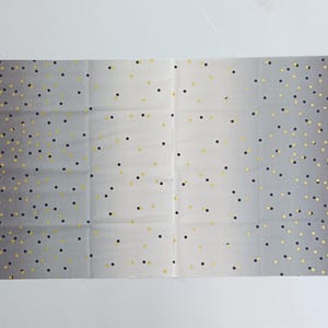 May include: A rectangular fabric with a gradient gray background, adorned with scattered black and gold polka dots. The dots are densely packed on the edges and gradually thin out towards the center. The fabric is folded into four sections.