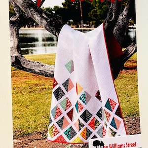 May include: A quilt pattern booklet titled Spellbound on Williams Street featuring a white quilt with a pieced diamond design in various colors including red, yellow, green, and black with white patterns, finished with a red border.