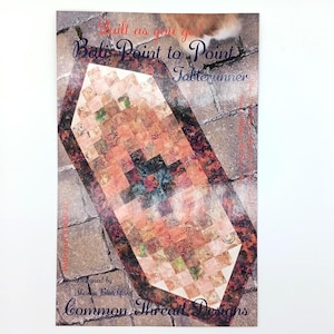 May include: A rectangular quilt pattern titled Quilt as you go! Bali Point to Point Tablerunner by Sharan Blatchford for Common Thread Designs. The cover features a patchwork tablerunner with orange, brown, and dark red tones on a stone background.