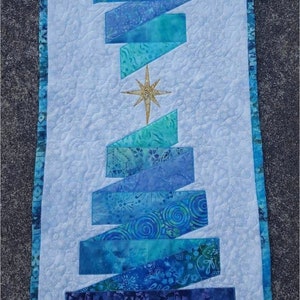 May include: A quilted wall hanging featuring a stylized Christmas tree design. The tree is composed of blue fabric rectangles with various patterns, set against a white background. A gold star adorns the center.