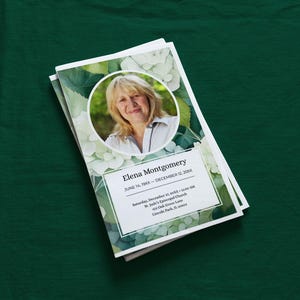 May include: A stack of memorial or funeral templates featuring a photo of a woman in a white circle, surrounded by a floral design. The text includes the name "Elena Montgomery" and dates, with event details.