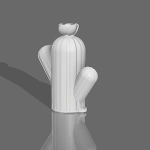 Puede incluir: Escultura de cactus de cerámica blanca con una parte superior redondeada y un solo brazo que se extiende hacia un lado. El cactus está de pie sobre una superficie gris.