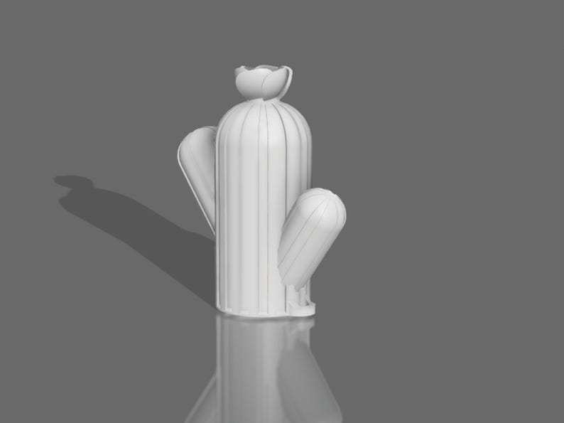 May include: White ceramic cactus sculpture with a rounded top and a single arm extending out to the side. The cactus is standing on a gray surface.