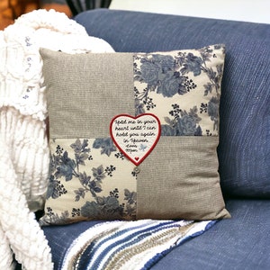 May include: A square pillow with a floral pattern in shades of blue and beige. The pillow has a red heart-shaped patch with the text "Hold me in your heart until I can hold you again in Heaven Love Mom" embroidered on it.