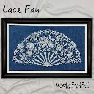 May include: A framed cross-stitch artwork featuring a white lace fan design on a blue background. The fan design includes floral and scrollwork details. The words "Lace Fan" are at the top, and "WorksByABC" is at the bottom.