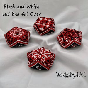 May include: Four small, red, black, and white hexagonal pincushions with geometric patterns. The pincushions are on a white fabric background. The text "Black and White and Red All Over" is at the top of the image. The text "WorksByABC" is at the bottom of the image.