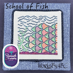 Puede incluir: Arte de punto de cruz titulado "School of Fish" que presenta una colorida escena submarina. El diseño incluye peces en tonos naranja, rosa y verde, con olas azules y algas verdes. La obra está enmarcada con tela azul y un borde de cuerda oscura.