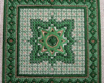 May include: A green and brown cross-stitch pattern with a starburst design in the center. The pattern is framed by a border of green and brown.