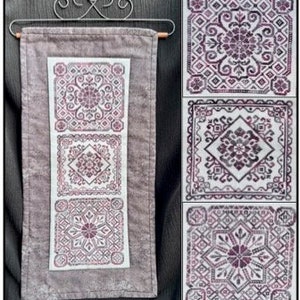 May include: Three embroidered squares in shades of purple and gray on a gray fabric background. The squares feature intricate geometric patterns.