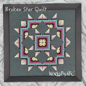 May include: A framed cross-stitch design of a "Broken Star Quilt" with a colorful geometric pattern in shades of pink, yellow, blue, black, and white. The design is framed in a black frame with the text "WorksByABC" in the bottom right corner.