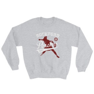 May include: A grey sweatshirt with a red vintage-style graphic of a baseball player and the text "Rockford Peaches 1943" with a registered trademark symbol.