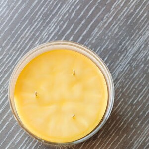 May include: A yellow candle in a clear glass jar with three wicks.