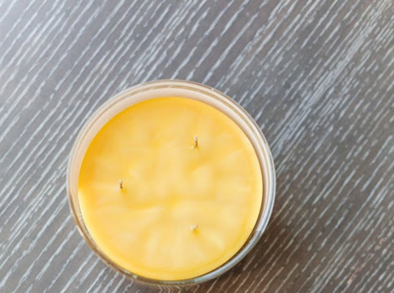 May include: A yellow candle in a clear glass jar with three wicks.