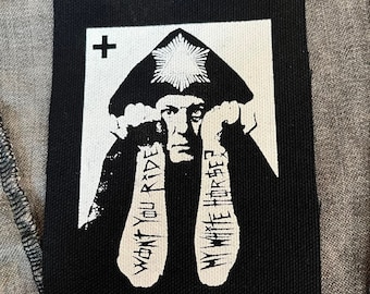 May include: A rectangular black and white fabric patch featuring a graphic illustration of a person wearing a pointed hat with a star. The text "WON'T YOU RIDE MY WHITE HORSE?" is printed on the person's sleeves, with a small cross in the corner.
