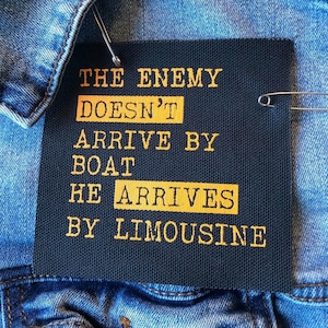 May include: Black canvas patch with gold text that reads "The enemy doesn't arrive by boat he arrives by limousine."