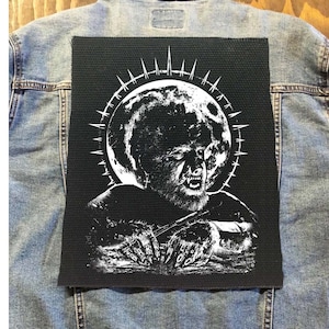 May include: Black and white embroidered patch featuring a werewolf howling at the moon. The werewolf is surrounded by a circle of spikes. The patch is sewn onto a denim jacket.