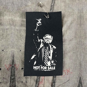 Może przedstawiać: Czarno-biała naszywka do prasowania przedstawiająca sylwetkę osoby podnoszącej pięść w górę. Osoba jest ubrana w garnitur i krawat. Tekst "NOT FOR SALE" jest nadrukowany pod obrazkiem.