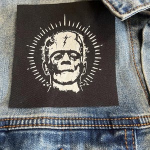 Peut inclure: Patch thermocollant noir avec un motif blanc de Frankenstein avec un &eacute;clair sur le front. Le monstre est entour&eacute; d'un cercle blanc avec des lignes rayonnantes.