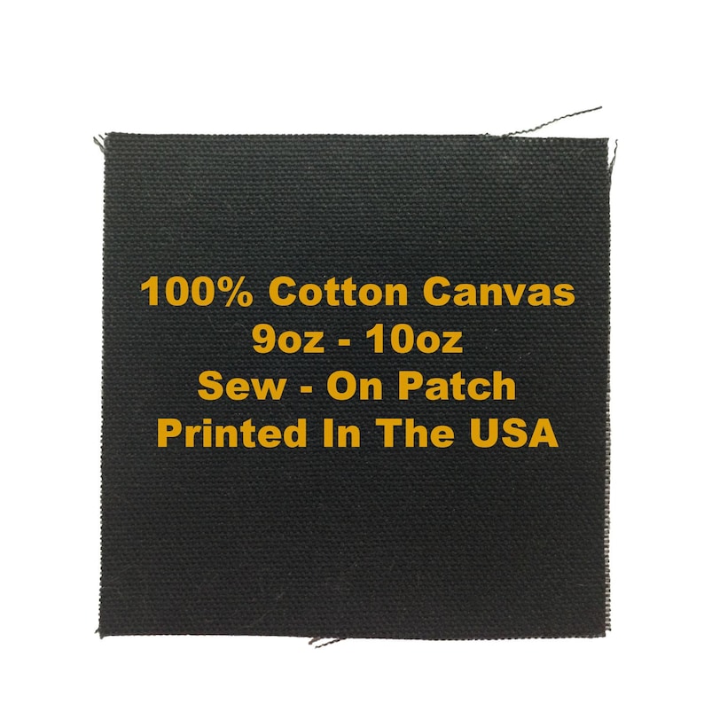 May include: A square black sew-on patch made of 100% cotton canvas. The patch features yellow text that reads: 100% Cotton Canvas, 9oz - 10oz, Sew - On Patch, Printed In The USA. The fabric has a visible woven texture with raw edges.