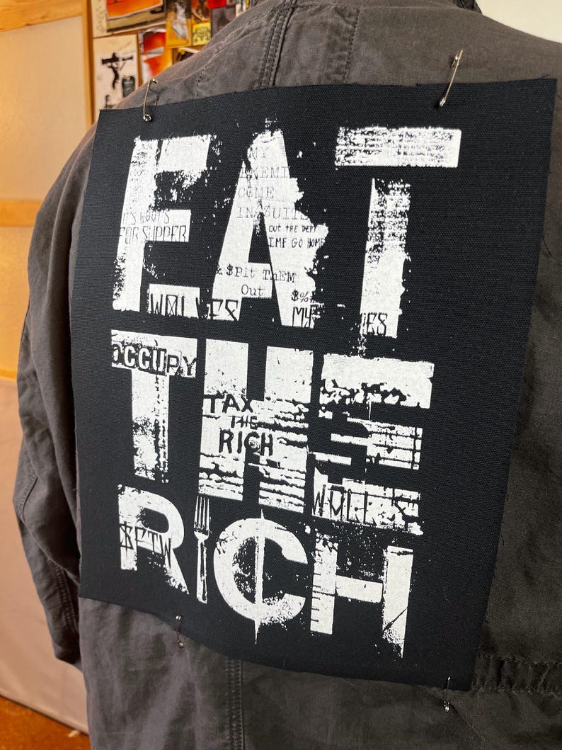 Pu&ograve; includere: Toppa in tessuto nero con testo bianco che recita "Eat the Rich" con altro testo che la circonda. Il testo &egrave; in uno stile usurato.