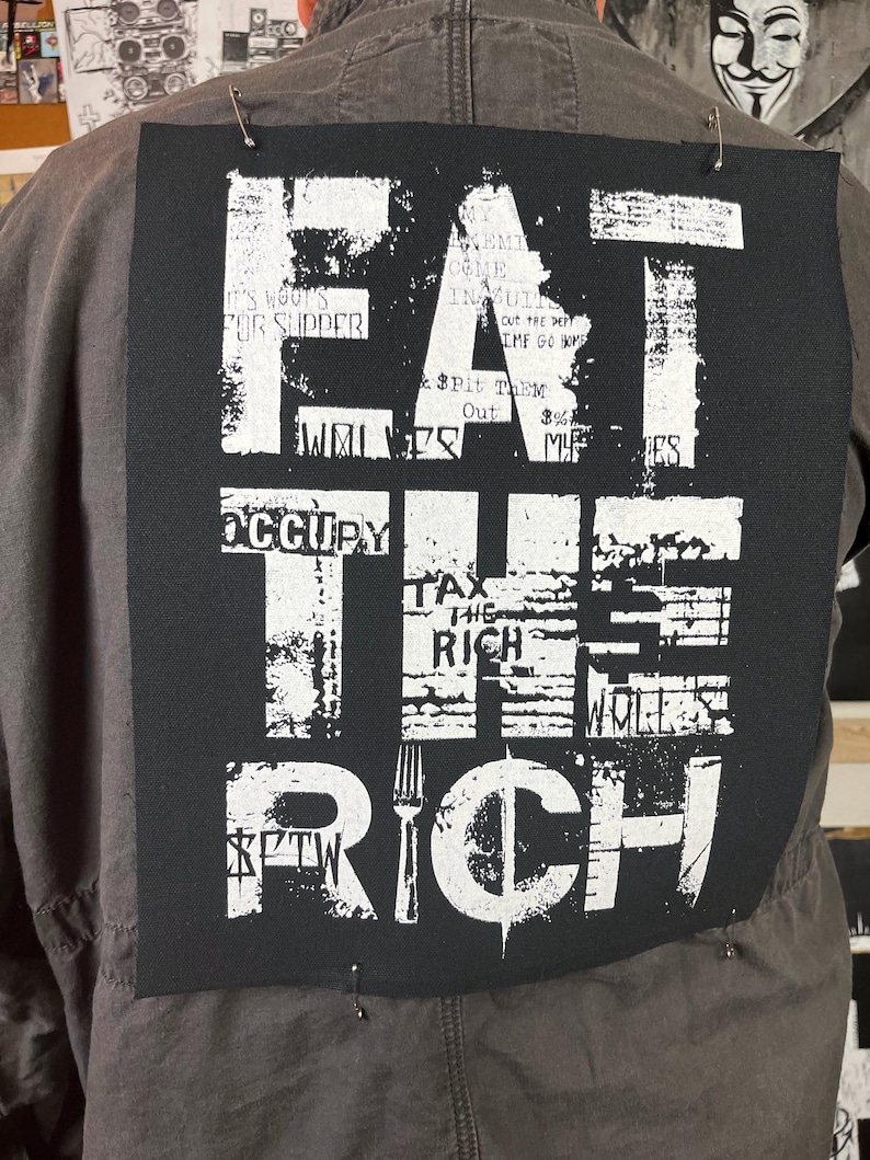 Pu&ograve; includere: Toppa nera e bianca con il testo "Eat the Rich" in un font usurato. La toppa ha una grafica di forchetta e simbolo del dollaro.