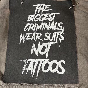 Oversized punk back patch with raw stencil lettering that says 'The Biggest Criminals Wear Suits Not Tattoos', made for battle jackets, anarchist style, and DIY rebellion.