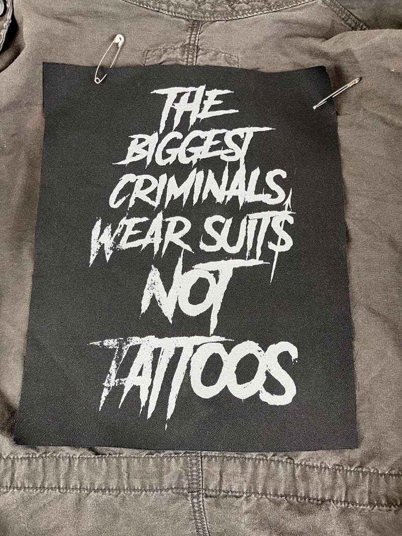 Oversized punk back patch with raw stencil lettering that says 'The Biggest Criminals Wear Suits Not Tattoos', made for battle jackets, anarchist style, and DIY rebellion.