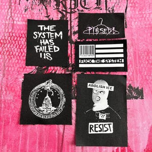 May include: Four rectangular black fabric patches with white screen-printed graphics. Designs include text reading THE SYSTEM HAS FAILED US, PISSED with a hanger icon, a barcode flag with FUCK THE SYSTEM, a snake over a building, and a person in a balaclava.