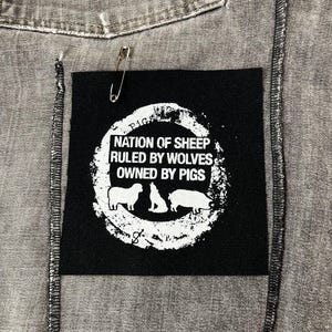 May include: Black patch with white text and graphic. The text reads "Nation of Sheep Ruled by Wolves Owned by Pigs". The graphic is a circle with a sheep, wolf, and pig inside.
