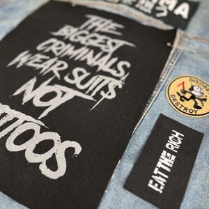 Oversized punk back patch with raw stencil lettering that says 'The Biggest Criminals Wear Suits Not Tattoos', made for battle jackets, anarchist style, and DIY rebellion.