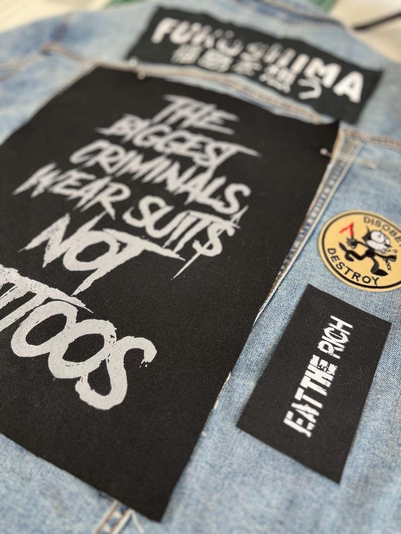Oversized punk back patch with raw stencil lettering that says 'The Biggest Criminals Wear Suits Not Tattoos', made for battle jackets, anarchist style, and DIY rebellion.