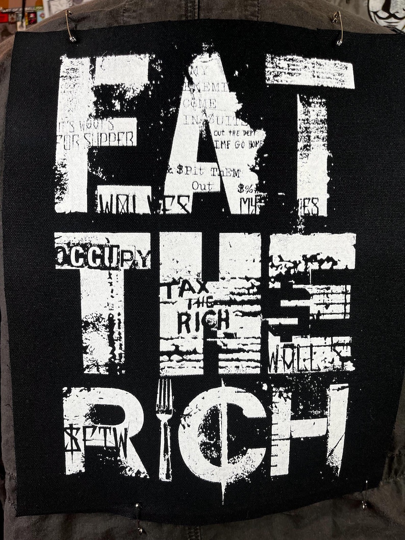 Pu&ograve; includere: Toppa bianca e nera con il testo "Eat the Rich" in un carattere audace e usurato. La toppa presenta una grafica di forchetta e dollaro. Sono visibili anche i testi "Occupy" e "Tax the Rich".