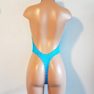 May include: A turquoise swimsuit with a halter neck and a low back. The swimsuit is adorned with small, clear rhinestones.