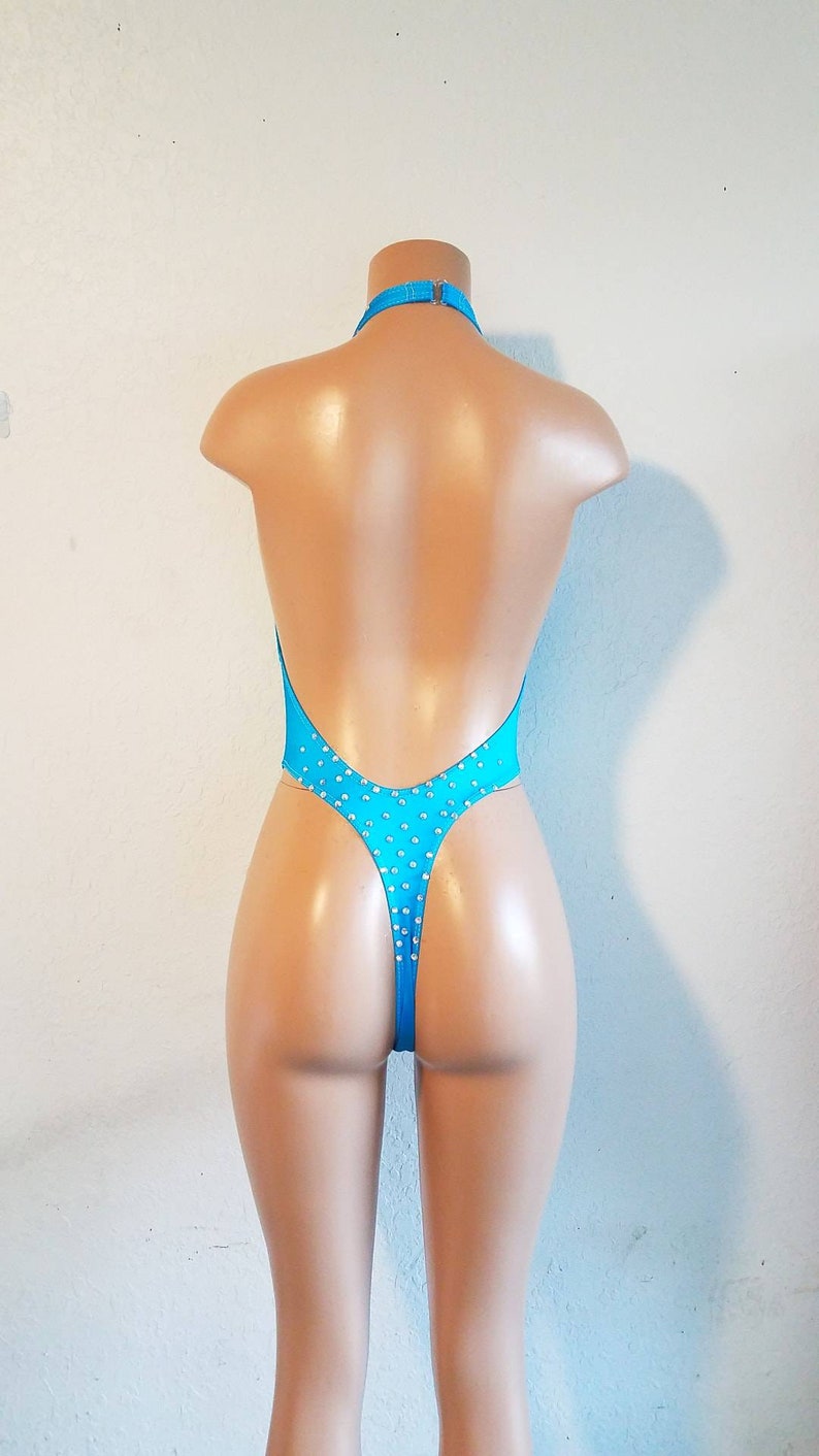 May include: A turquoise swimsuit with a halter neck and a low back. The swimsuit is adorned with small, clear rhinestones.