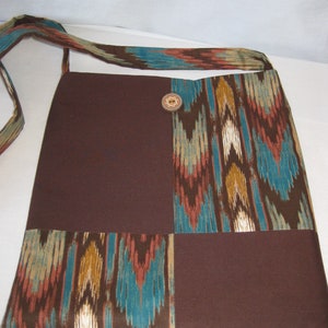 K&ouml;nnte beinhalten: Eine braune und t&uuml;rkisfarbene Patchwork-Tragetasche mit geometrischem Muster. Die Tasche hat einen braunen Trageriemen und einen dekorativen Knopf.