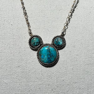 Pu&ograve; includere: Collana argentata con tre pietre turchesi. La pietra centrale &egrave; pi&ugrave; grande, con due pietre pi&ugrave; piccole su entrambi i lati, il tutto incastonato in una cornice d'argento decorativa. La catena &egrave; delicata.