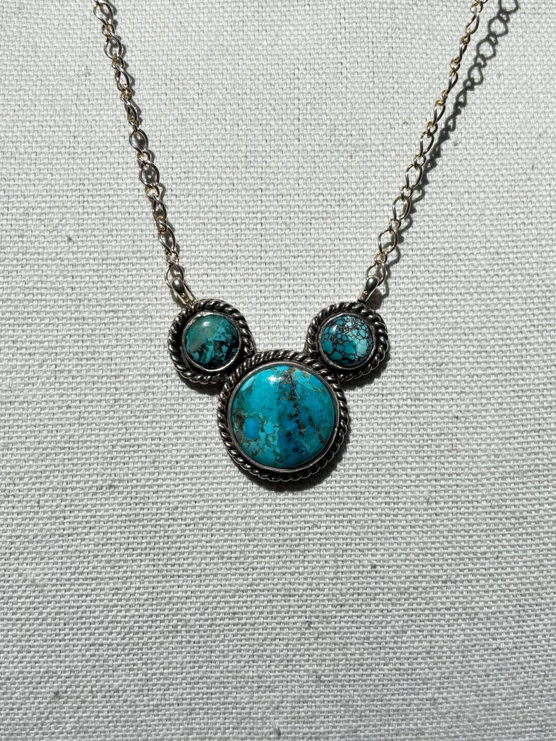Pu&ograve; includere: Collana argentata con tre pietre turchesi. La pietra centrale &egrave; pi&ugrave; grande, con due pietre pi&ugrave; piccole su entrambi i lati, il tutto incastonato in una cornice d'argento decorativa. La catena &egrave; delicata.